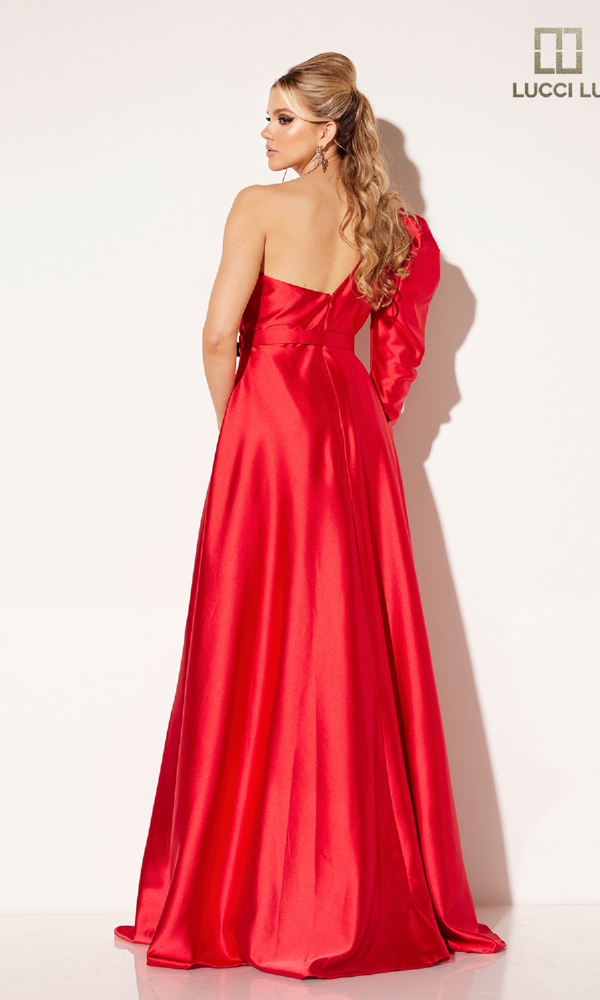 A woman stands with her back to the camera in a shiny, floor-length red Lucci Lu C8098 formal dress featuring an A-line silhouette and one-shoulder design, set against a plain white background.